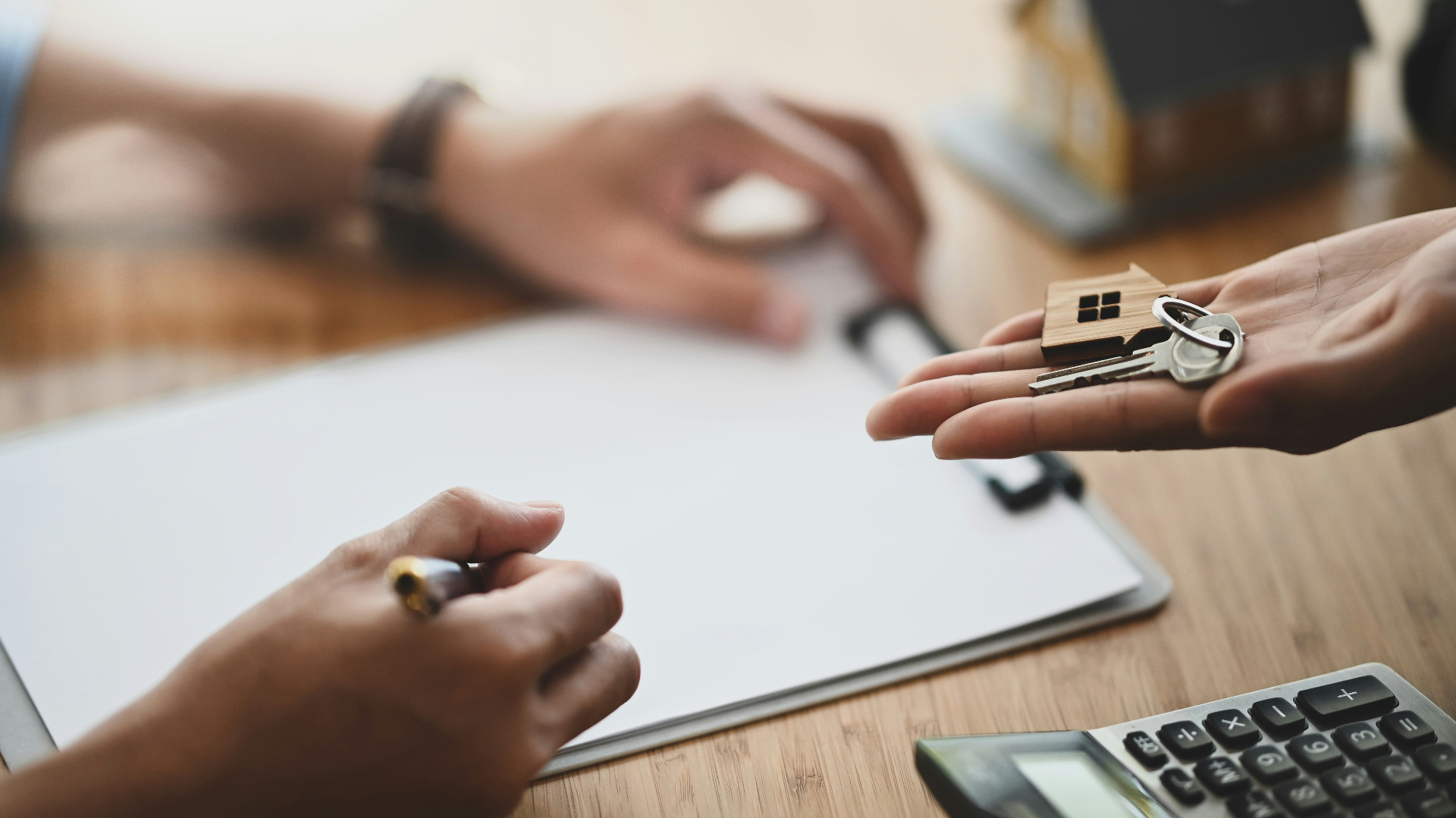 Real estate advisor handing house keys across a desk with a clipboard and calculator, illustrating the financing decisions behind every Austin property transaction