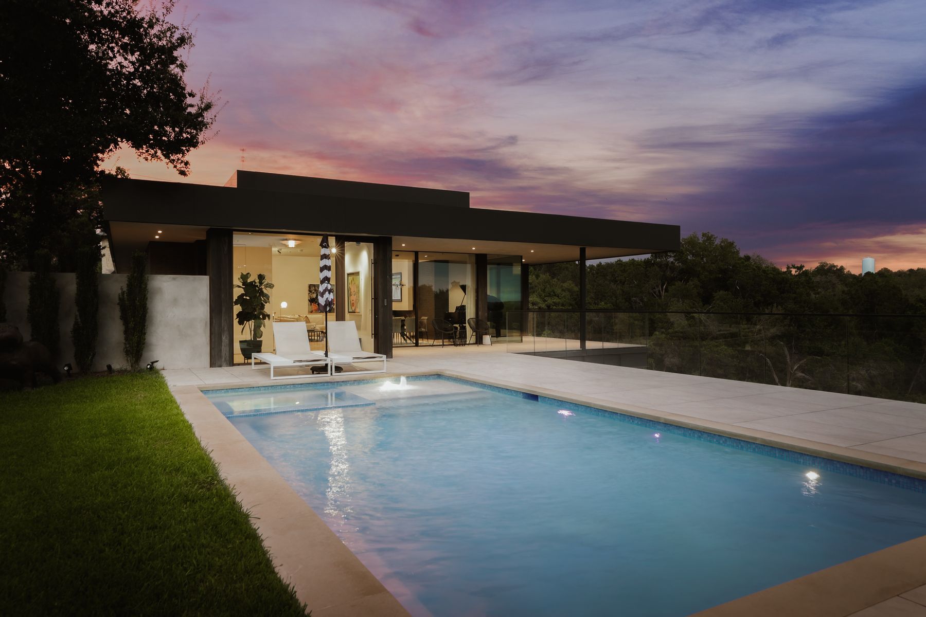 The Eanes Premium: What Austin Buyers Really Pay for Westlake Schools, and Whether It Holds in 2026 Modern minimalist West Austin home with a glowing pool at dusk, floor-to-ceiling glass doors open to an open-concept living and dining area under a purple-pink sky