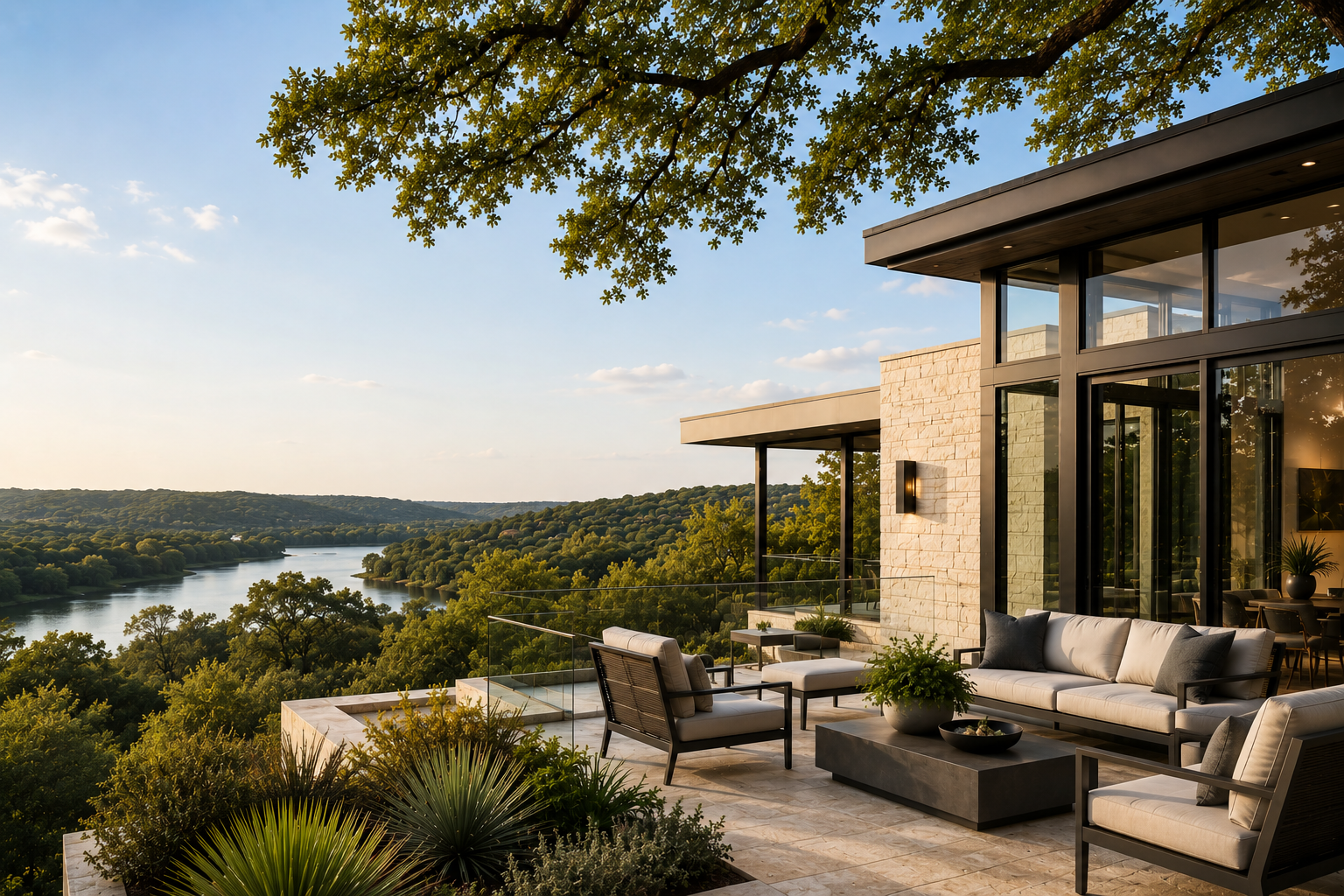 Modern luxury home terrace in Westlake Hills at golden hour overlooking Lake Austin and the surrounding Texas Hill Country, with a stone and glass residence, contemporary outdoor seating, and mature live oaks framing the view