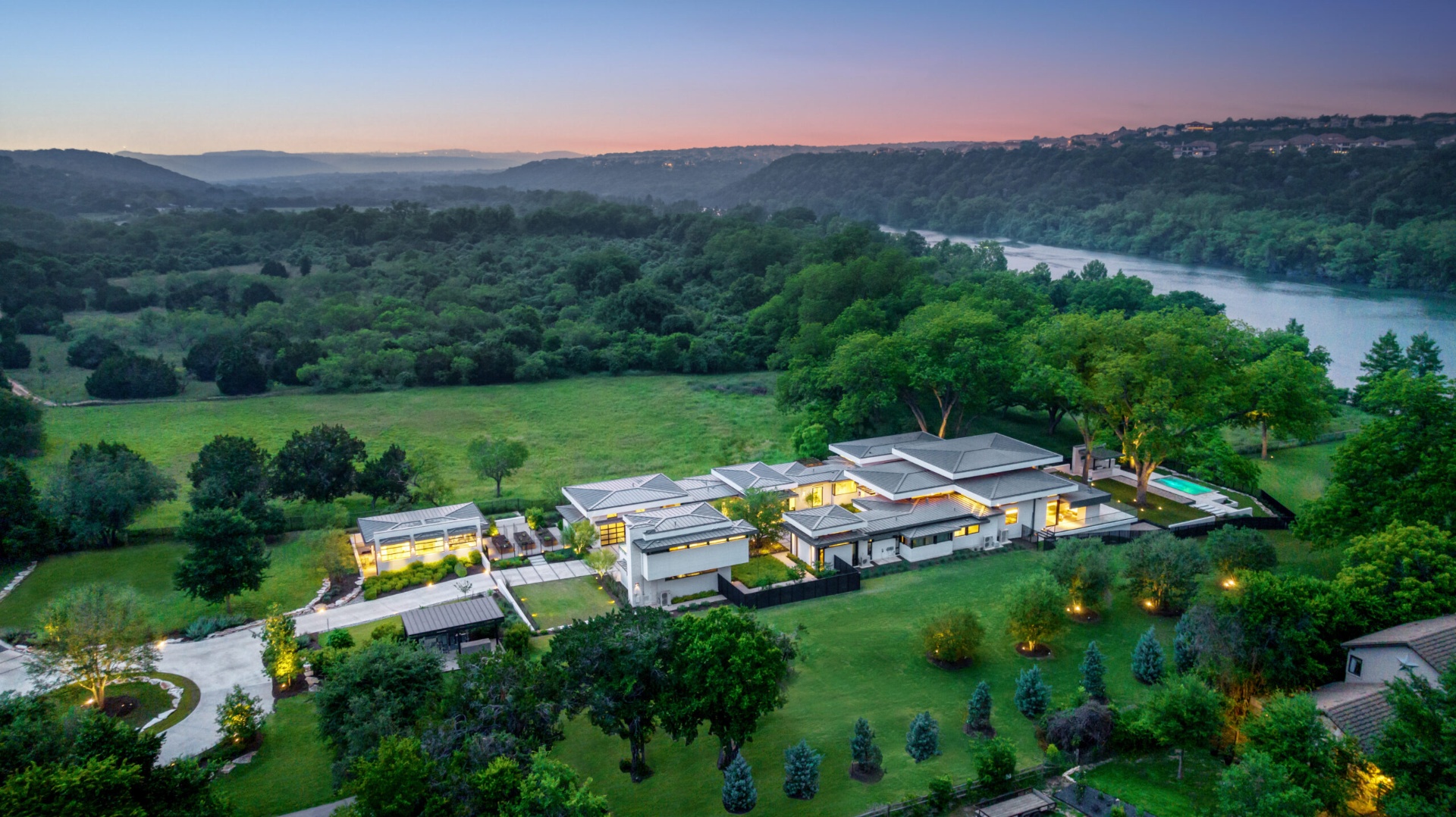 Aerial twilight view of a modern West Austin estate set above the Colorado River with the Hill Country ridgeline in the distance