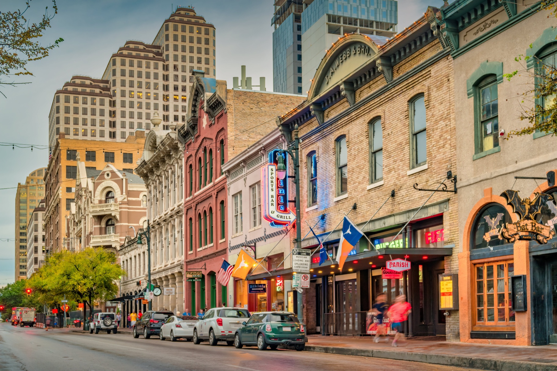 Historic Sixth Street storefronts and the downtown Austin skyline at dusk, illustrating the city's mix of neighborhoods and price tiers behind inventory data